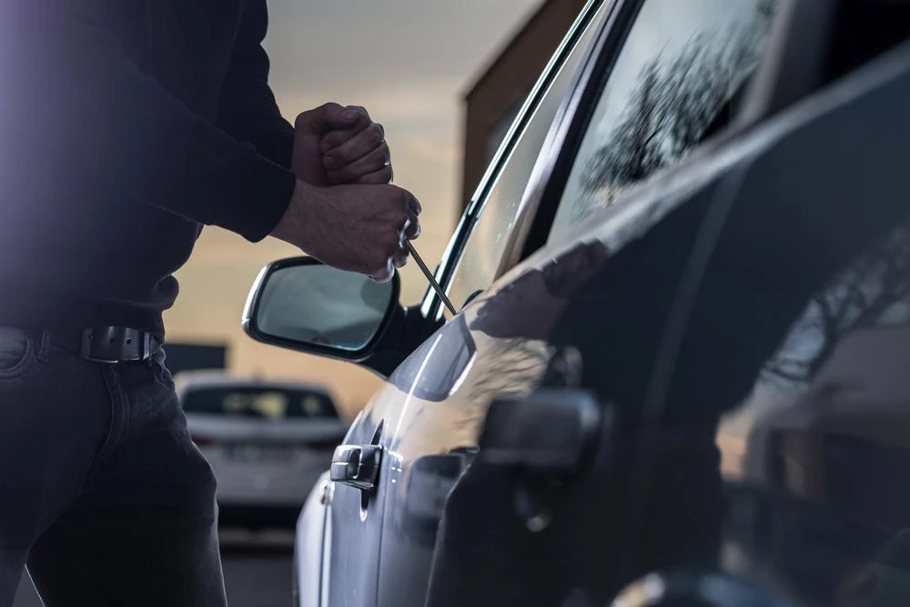 Auto thief in black balaclava trying to break into car with screwdriver