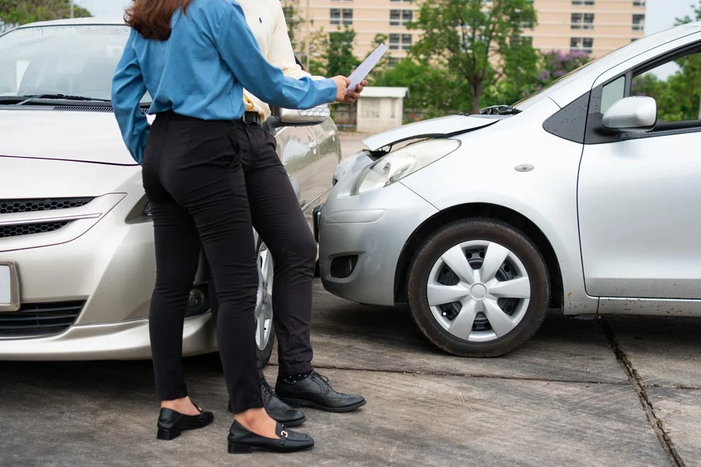 Two Drivers using a smartphone to exchange phone numbers and social media after a car accident.
