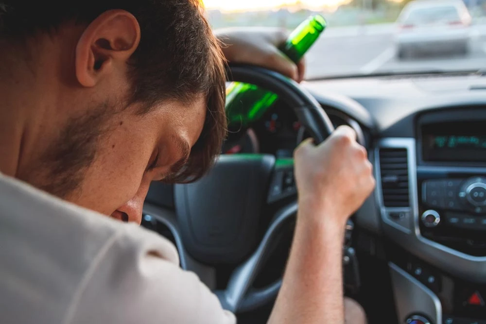Drunk young man driving a car with a bottle of beer. Don't drink and drive concept